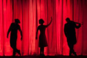 Three performers are performing against a red curtain showing that It only happens in the movies quotes.