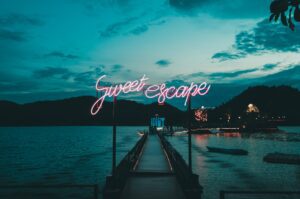 This is an image of a bridge and an ocean with a neon sign written, Sweet Escape and these words are also used in the Poem, Whhich one is