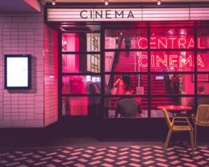 The is an image of a cafe written cinema and a girl is sitting besides window. This picture is talking about the impact of media in promoting romance. 